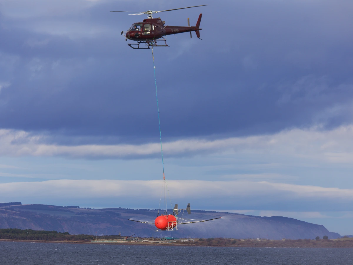 Helicopter with underslung dispersant spray system flying low over an estuary