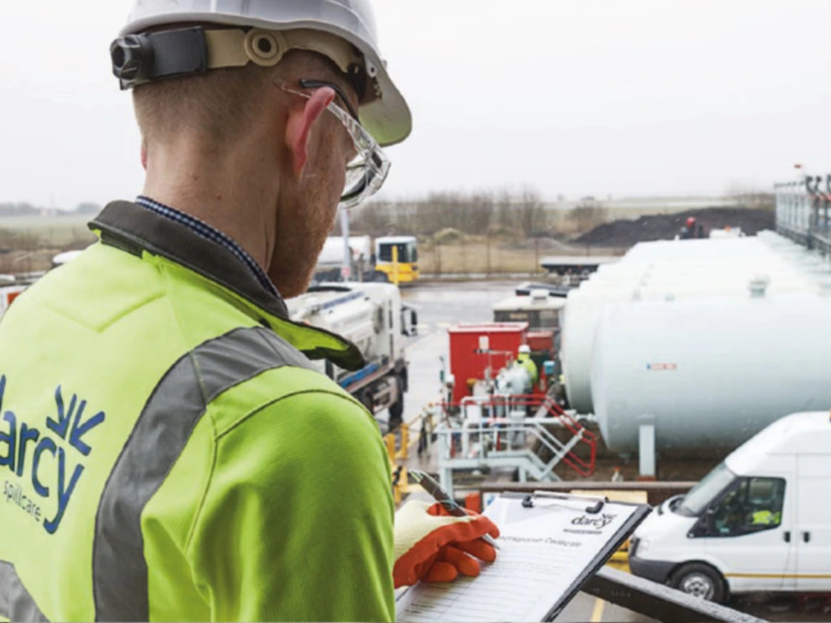 Darcy team member wearing high-visibility clothing and a hard hat completes a checklist overlooking an industrial tank storage site.